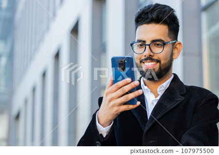 Smiling business man using smartphone typing text answering messages chatting online in city street 107975500