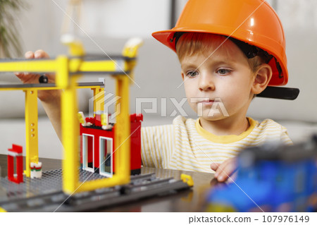 Child boy in helmet playing and building with colorful plastic bricks at table Child boy in helmet playing and building with colorful plastic bricks at table 107976149