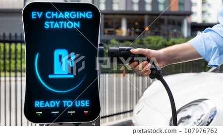 Businessman pull and hold EV charger plug form charging station. Peruse Businessman pull and hold EV charger plug form charging station. Peruse 107976762