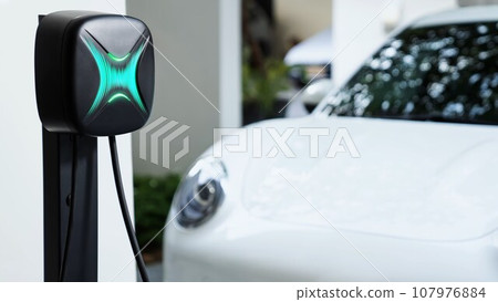 Electric car plugged in with home charging station. Peruse 107976884