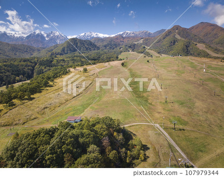 Snow-capped Hakuba Sanzan and three-tiered autumn leaves at Tsugaike Kogen Ski Resort, Otari Village, Nagano Prefecture (aerial shot by drone) 107979344