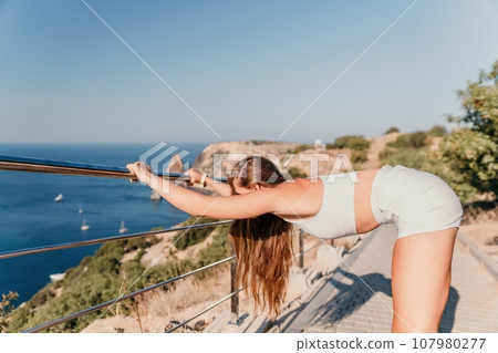 Fitness woman sea. Outdoor workout in park over beach. Female fitness pilates yoga routine concept. Healthy lifestyle. Happy fit woman exercising with rubber band in park. 107980277