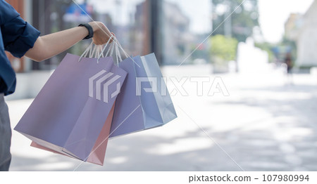 Close up of woman hand holding shopping bags while walking near mall 107980994