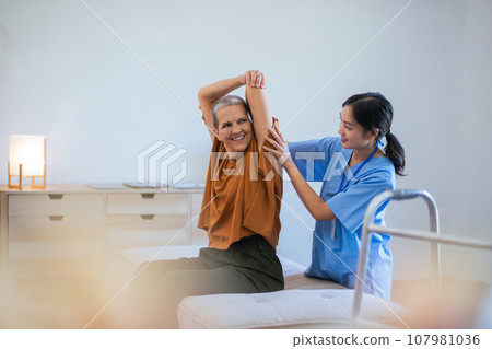 Physical therapist caregiver Asian and Caucasian senior women trust moving hand in rehabilitation. Physiotherapy healthcare, Medical caregiver consulting disabled elderly patient at home 107981036