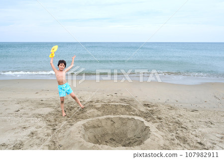 Children dig a hole in the sand on the seashore. 107982911
