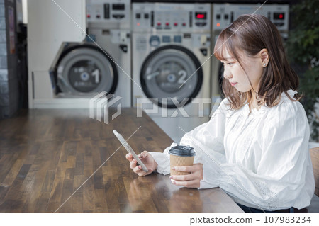 Young woman waiting for laundry to finish at a laundromat Young woman waiting for laundry to finish at a laundromat 107983234