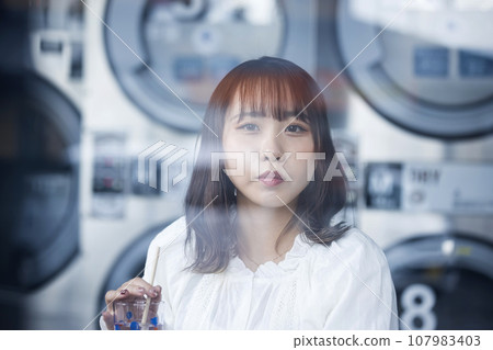年輕女子在自助洗衣店喝杯茶，等待選擇完成 107983403