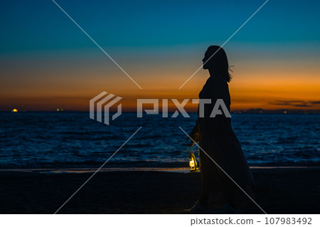 A young woman walks with a lantern in hand in the gradation of sunset 107983492