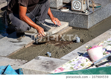 A craftsman who performs maintenance work on a grave inside a cemetery. A craftsman who performs maintenance work on a grave inside a cemetery. 107984559