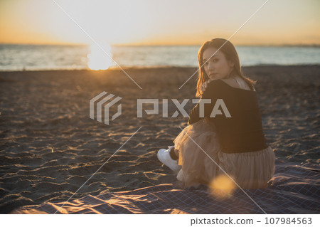 Reflection of a woman sitting on the beach at sunset 107984563