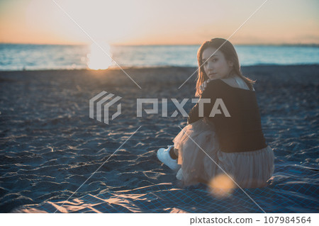 Reflection of a woman sitting on the beach at sunset. teal & orange 107984564
