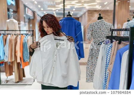 Shopping woman, women's fashion clothes in a store, boutique. Woman choosing clothes in a store 107984884