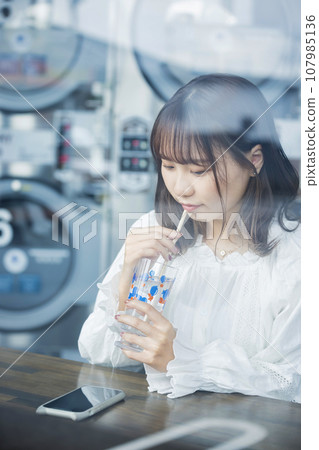 Young woman having tea at the laundromat 107985136