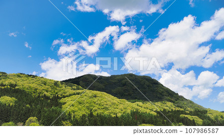 Sunny blue sky, clouds, and fresh green mountain scenery Sunny blue sky, clouds, and fresh green mountain scenery 107986587