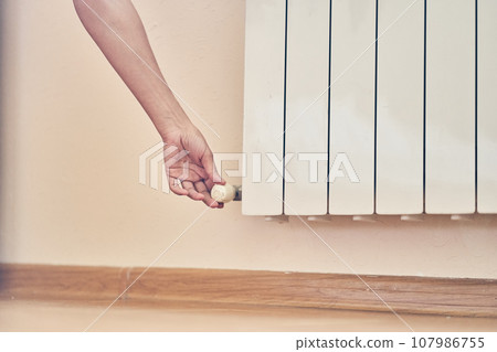 A woman's hand regulating the temperature on the radiator. The concept of the energy crisis in Europe with space to copy. High quality photo 107986755