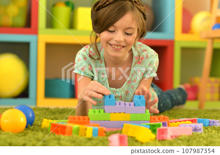 Portrait of cute girl playing with colorful plastic blocks in room 107987354