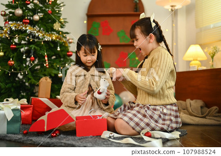 Surprised cute little children opening Christmas present in decorated living room Surprised cute little children opening Christmas present in decorated living room 107988524
