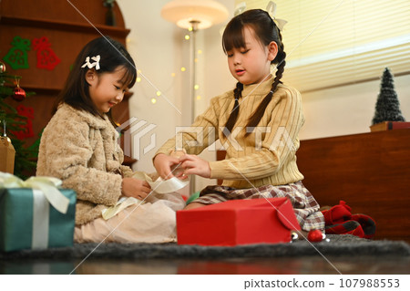 Two happy siblings sitting on floor in beautiful festive living room unpacking Christmas gift boxes Two happy siblings sitting on floor in beautiful festive living room unpacking Christmas gift boxes 107988553