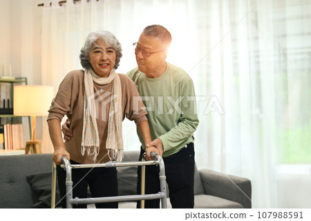 Caring senior man helping his wife walking with walker at home. Elderly healthcare concept 107988591