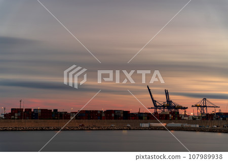 Bustling Commercial Dock at Dusk with Containers and Cranes 107989938