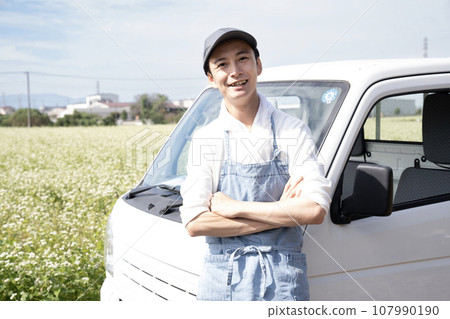 A field of buckwheat noodles, a light truck, and a farmer man wearing a hat 107990190