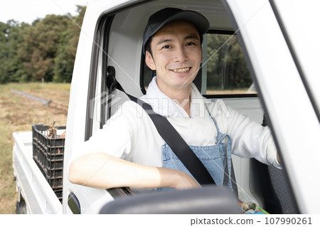 A farmer man sitting in the driver's seat of a light truck A farmer man sitting in the driver's seat of a light truck 107990261