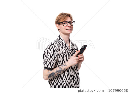 young caucasian guy with red hair dressed in a shirt holds a phone in his hand 107990668