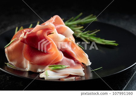 Prosciutto with rosemary on a black plate. Prosciutto with rosemary on a black plate. 107991160