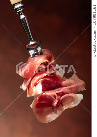 Prosciutto on a fork. 107991161