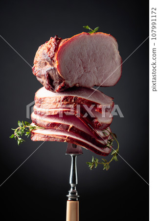 Sliced smoked gammon with thyme branches on a fork. 107991172