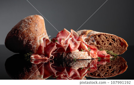 Prosciutto with ciabatta and thyme on a black background. Prosciutto with ciabatta and thyme on a black background. 107991192