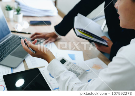 Young economists or accountants or financiers and investors are reviewing budget documents and using computers to study impact and risk assessments on corporate investment management. 107992278
