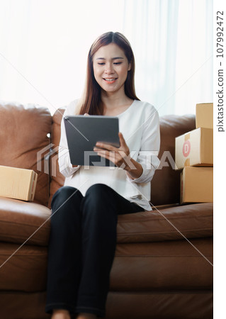Starting small business entrepreneur of independent young Asian woman online seller is using tablet computer and taking orders to pack products for delivery to customers. SME delivery concept. Starting small business entrepreneur of independent young Asian woman online seller is using tablet computer and taking orders to pack products for delivery to customers. SME delivery concept. 107992472