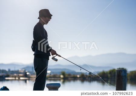 Young man enjoying fishing early in the morning on a sunny day Young man enjoying fishing early in the morning on a sunny day 107992623
