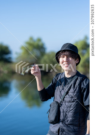 Young man enjoying fishing early in the morning on a sunny day Young man enjoying fishing early in the morning on a sunny day 107992635