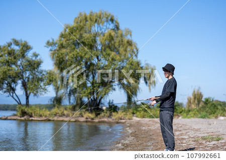 Young man enjoying fishing early in the morning on a sunny day Young man enjoying fishing early in the morning on a sunny day 107992661