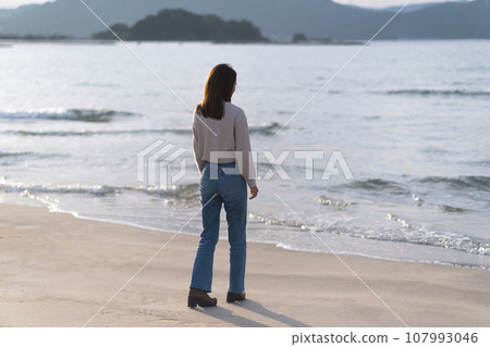 秋天，穿著喇叭牛仔褲在沙灘上行走的女子（福井縣若狹和田海灘） 107993046