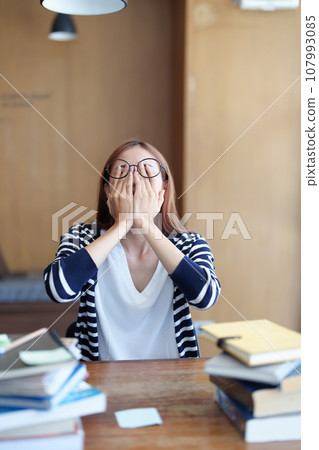 A portrait of an Asian teenage girl showing headaches and discouragement from studying in the library. 107993085