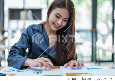 Portrait of an Asian female employee using a calculator to calculate corporate income tax to submit evidence to the Revenue Department before the end of the year. 107993086