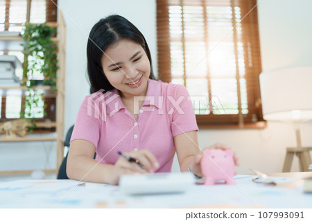 investment plan, young asian woman keep coin money in jar and using calculator to calculate savings. 107993091