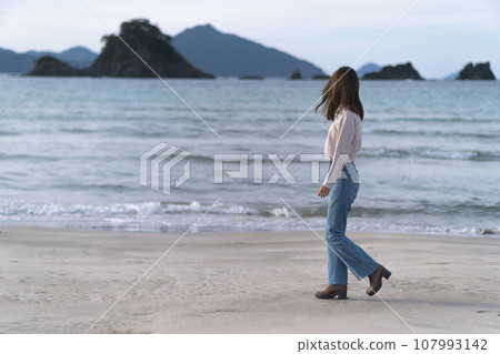 秋天，穿著喇叭牛仔褲在沙灘上行走的女子（福井縣若狹和田海灘） 107993142