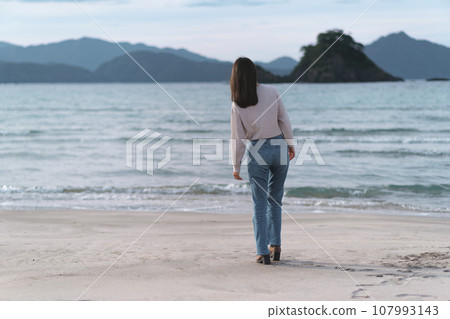 秋天，穿著喇叭牛仔褲在沙灘上行走的女子（福井縣若狹和田海灘） 107993143