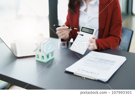 Guarantee, mortgage, contract, contract, signed, real estate agent or bank officer holding a calculator, submits a bid with a customer to buy a home before signing to make a deal. 107993301