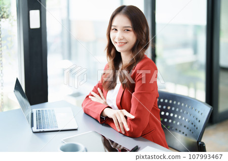 Portrait of a woman business owner showing a happy smiling face as he has successfully invested her business using computers and financial budget documents at work. Portrait of a woman business owner showing a happy smiling face as he has successfully invested her business using computers and financial budget documents at work. 107993467