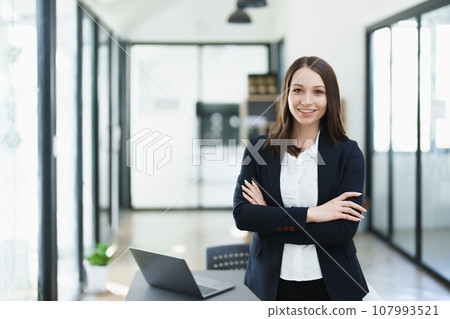 Portrait of a woman business owner showing a happy smiling face as he has successfully invested her business using computers and financial budget documents at work. 107993521