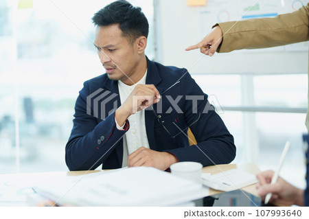 An image of an Asian male employee looking worried and sad about being scolded by his boss for failing to meet sales targets, concept of disappointment and failure in his career. 107993640