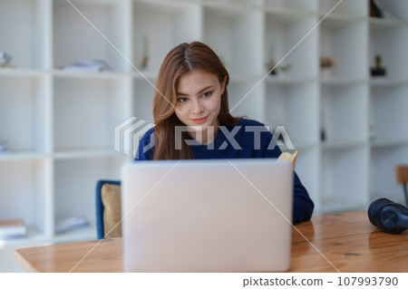 Happy latin girl college student watching distance online learning class, remote university webinar or having talk on laptop video call and use notebook to virtual meeting seminar at home or campus Happy latin girl college student watching distance online learning class, remote university webinar or having talk on laptop video call and use notebook to virtual meeting seminar at home or campus 107993790