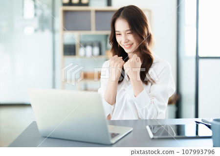 Portrait of a woman business owner showing a happy smiling face as he has successfully invested her business using computers and financial budget documents at work. Portrait of a woman business owner showing a happy smiling face as he has successfully invested her business using computers and financial budget documents at work. 107993796