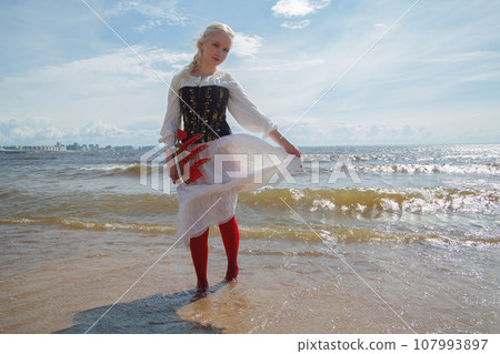 Nice woman in vintage dress holding red sail boat against sea and sky Nice woman in vintage dress holding red sail boat against sea and sky 107993897