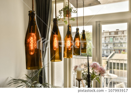 some wine bottles hanging from the ceiling over a dining room table with flowers in vases and candles on it some wine bottles hanging from the ceiling over a dining room table with flowers in vases and candles on it 107993917